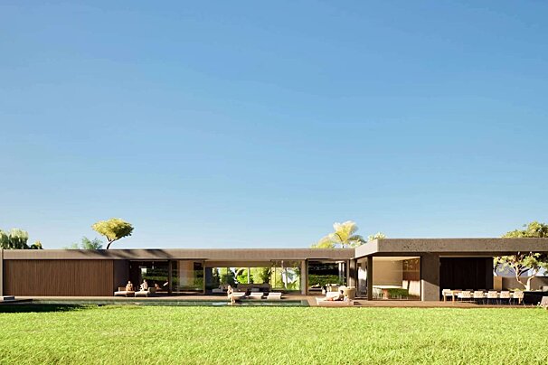 A sprawling modern home with glass walls, a pool, and outdoor lounging areas, set on a lush green lawn under a clear blue sky.