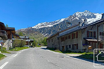 A winding road through an alpine village with traditional buildings and snow-capped mountains under a clear blue sky.