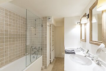 Modern bathroom featuring a bathtub with a glass screen and a white double-sink vanity with wood-framed mirrors.