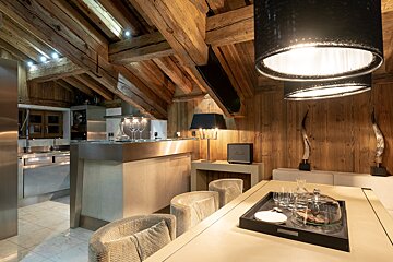 Cozy, modern-rustic kitchen and dining area with exposed wooden beams, sleek stainless steel accents, and stylish lighting.