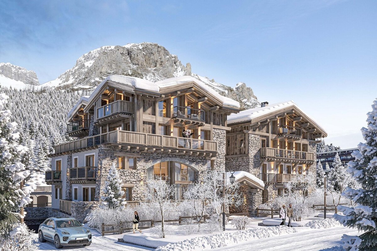 Luxurious stone and wood alpine chalets stand majestically in a pristine snowy mountain setting with frosted trees, a car, and people.