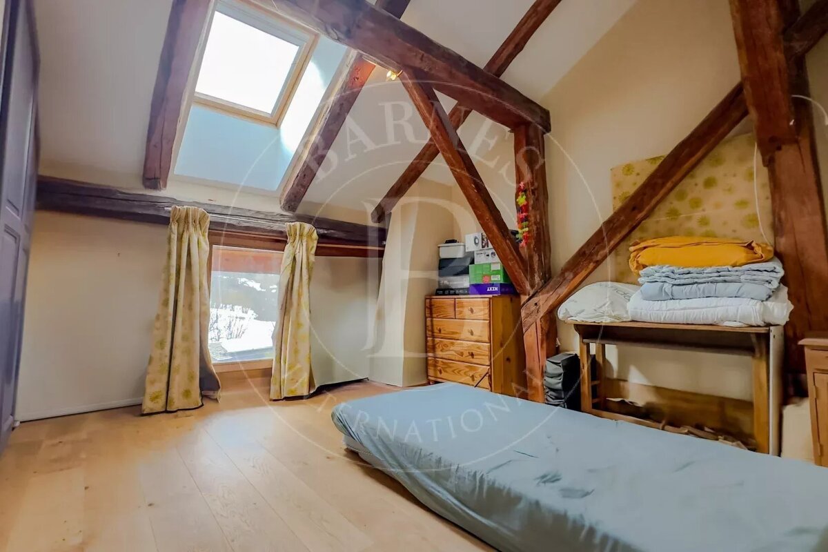 Cozy attic room with exposed wooden beams, a skylight, and a window overlooking a snowy scene. Features a mattress on the floor and wooden furniture.