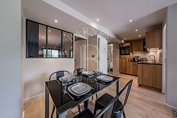 Modern open-plan kitchen and dining area featuring a sleek black table set for four, adjacent to a compact kitchen with light wood cabinets and a glass partition.