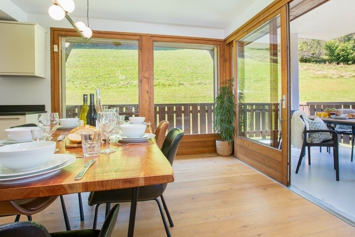 Bright dining area with a set wooden table, sliding glass doors, and a scenic view of a green hill.