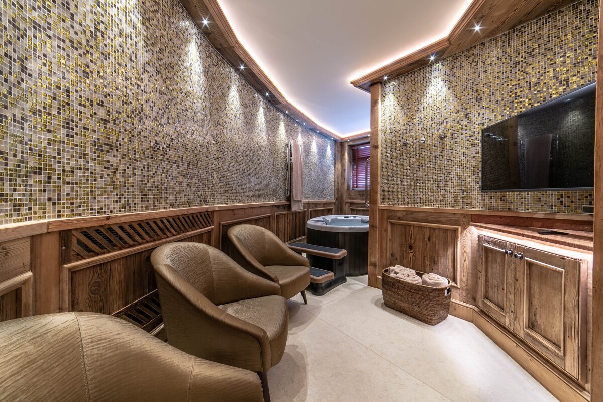 Luxurious spa room with mosaic walls, rustic wood accents, a hot tub, plush chairs, and ambient lighting, creating a relaxing atmosphere.