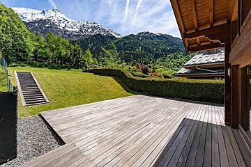 Wooden deck of a chalet overlooking a green lawn and stunning snow-capped mountains.