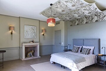 A chic bedroom with a bed, a fireplace featuring a leopard statue, a decorative fabric ceiling canopy, and unique lighting.
