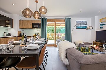 A stylish open-concept living and dining area featuring a set table, chic pendant lights, cozy sofa, and glass sliding doors.