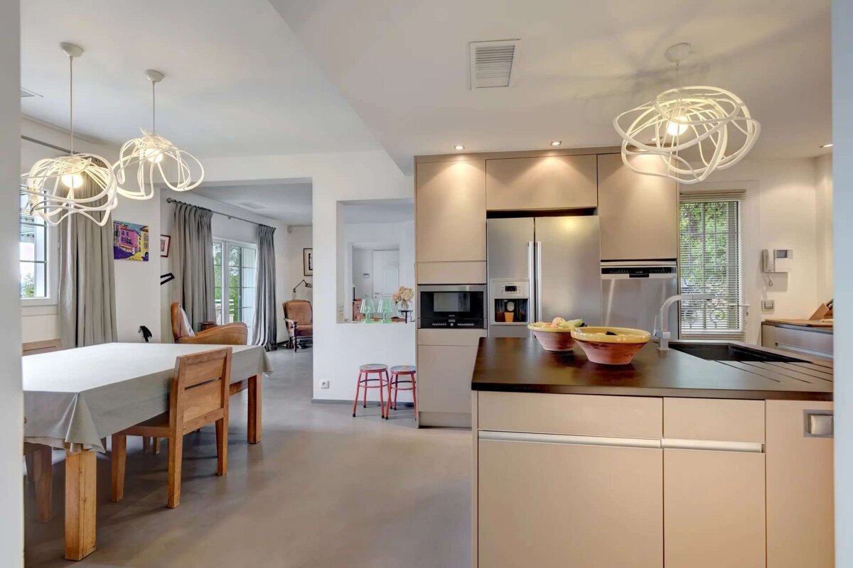 Modern, open-plan kitchen and dining room with light cabinets, stainless steel appliances, and sculptural pendant lights.