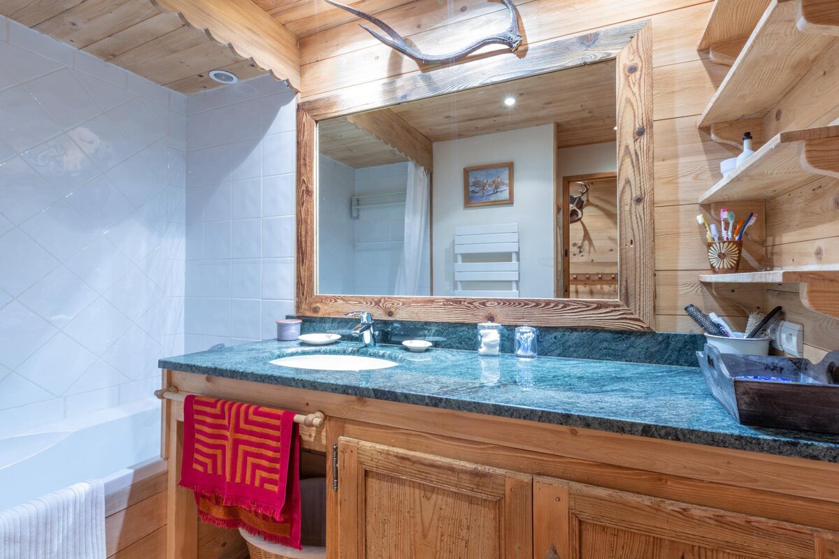Rustic bathroom featuring a wooden vanity with a green marble countertop, a large wood-framed mirror, and wood-paneled walls.