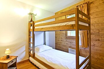 A bunk bed in a wooden room with a lamp on the nightstand