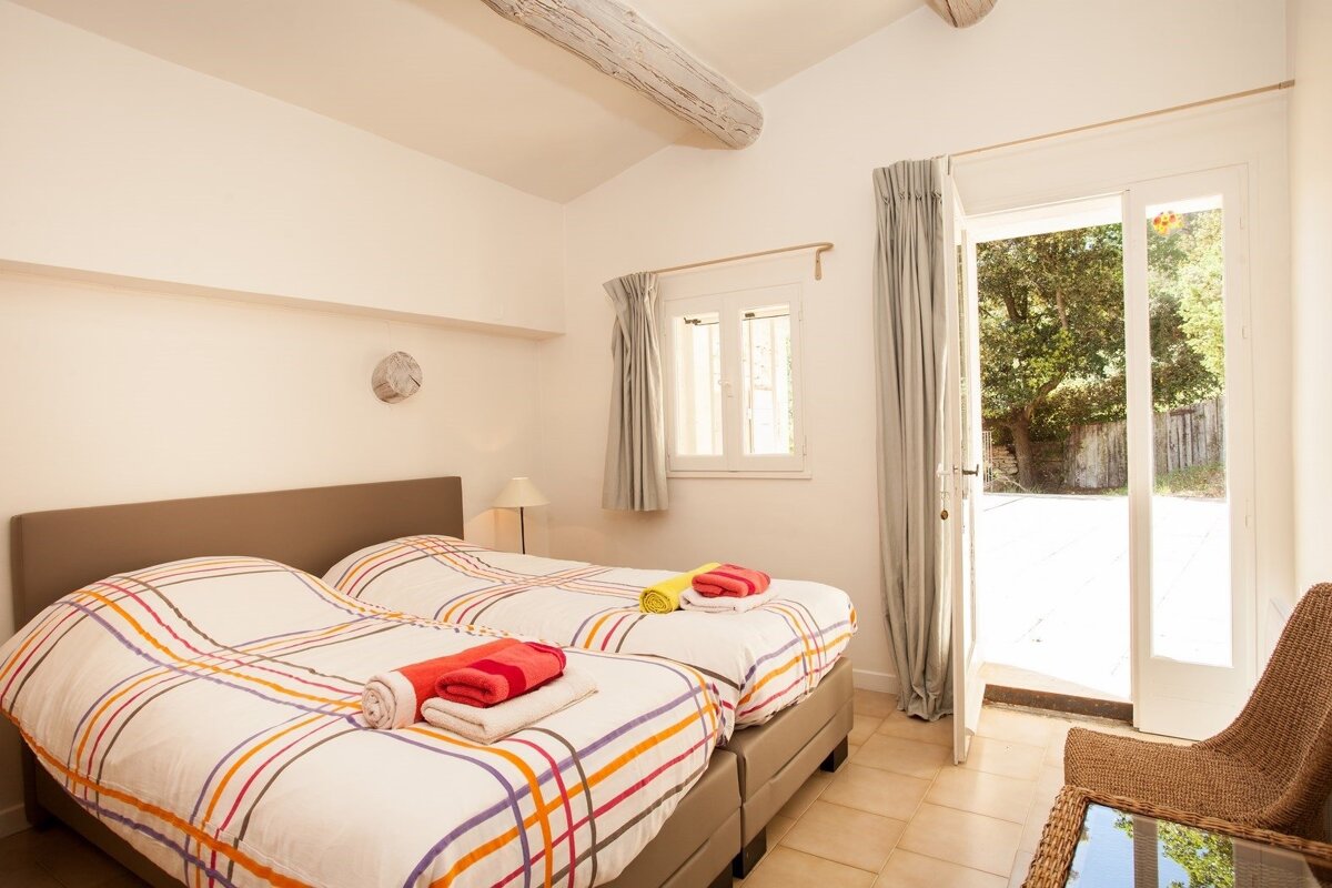 A bedroom with two beds and a wicker chair