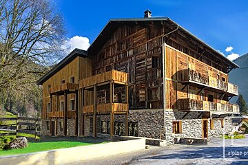 A rustic multi-story wooden chalet with stone foundation and balconies stands under a bright blue sky, surrounded by mountains and trees.