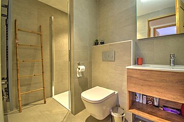 Modern, tiled bathroom featuring a shower, floating toilet, wooden vanity with sink, mirror, and a decorative bamboo ladder.