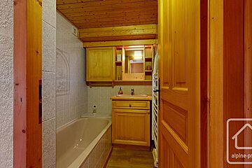 A cozy bathroom with a wooden ceiling, vanity, and door, featuring a bathtub, tiled walls, and a mirror cabinet.