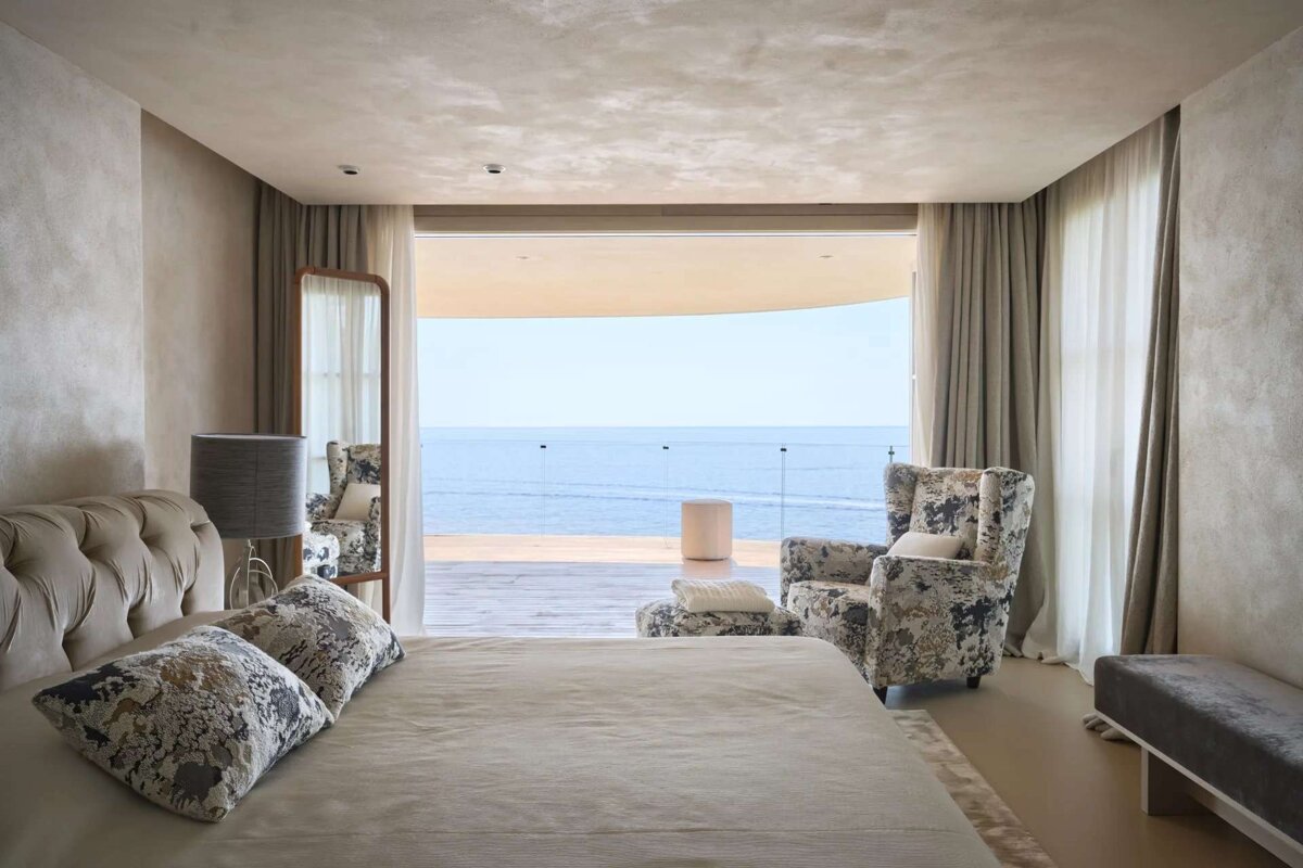 A bedroom with a large bed and chairs with a view of the ocean