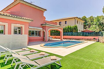Sunny pink villa with a blue swimming pool, multiple sun loungers on artificial grass, and a covered patio area, all under a clear sky.