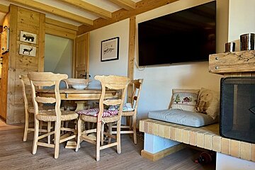 Cozy rustic dining room with a wooden table, chairs, wall-mounted TV, and a brick fireplace bench with decorative pillows.