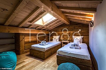 Cozy wooden attic bedroom with exposed beams, a skylight, and two twin beds with white linens.