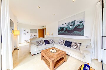 A modern living room features a large L-shaped sofa, wooden coffee table, and oversized rock art. White walls and light floors enhance the bright, open space.