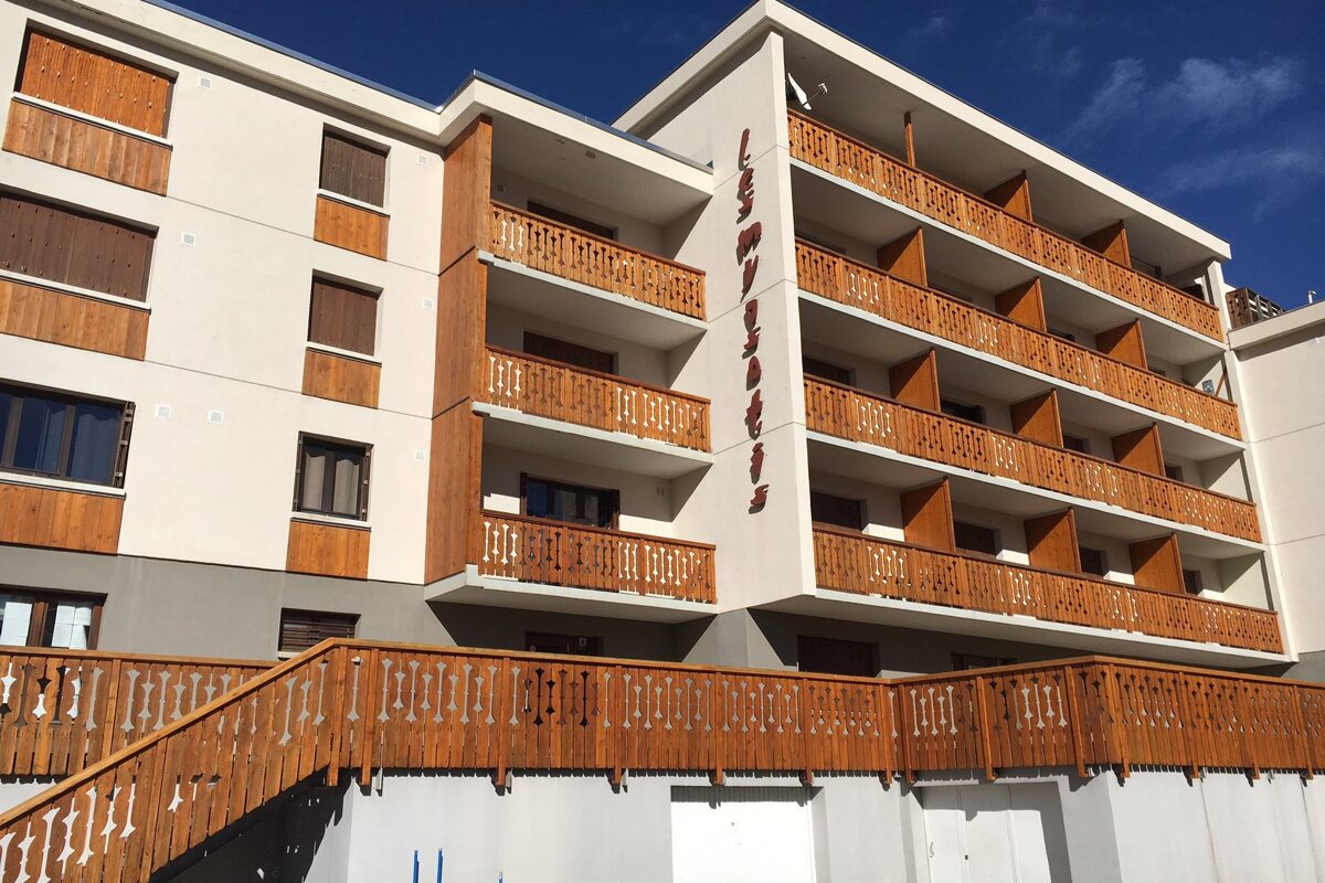 A white building with wooden balconies and the word les montagnes on the side