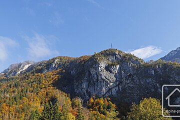 Majestic mountains ablaze with autumn colors, featuring rocky cliffs and a transmission tower on a peak, all beneath a clear blue sky.