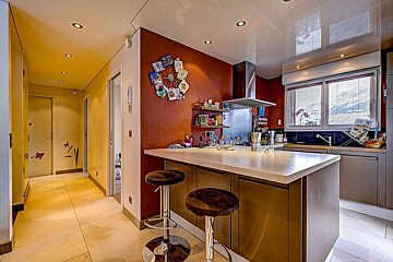 A modern kitchen with a red wall, island, bar stools, stainless steel appliances, and a bright hallway with fish decals.