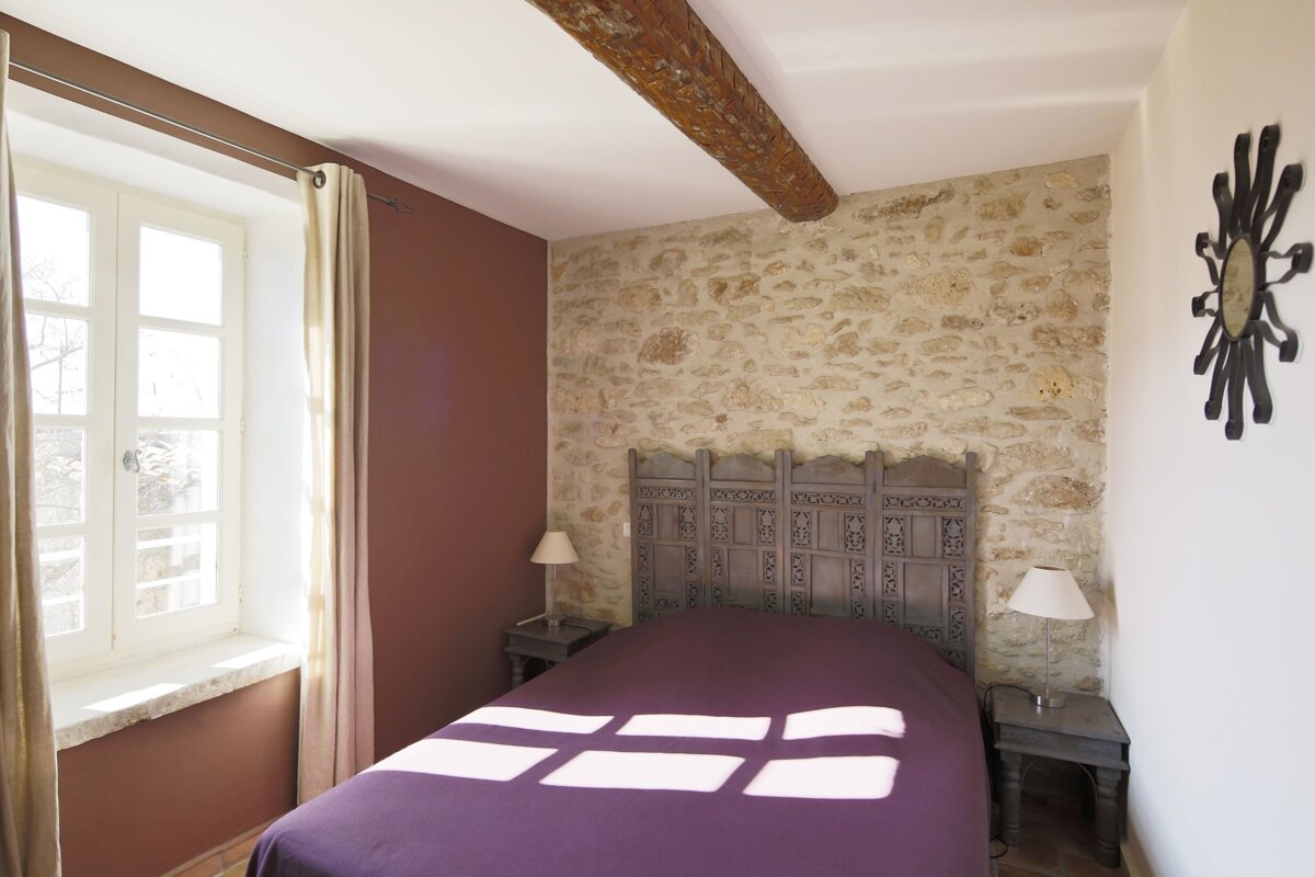 A bedroom with a stone wall and a purple bed