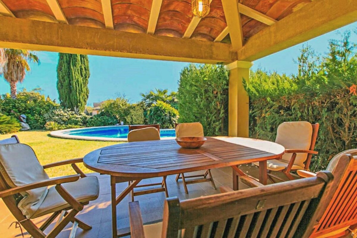 A patio with a table and chairs and a pool in the background