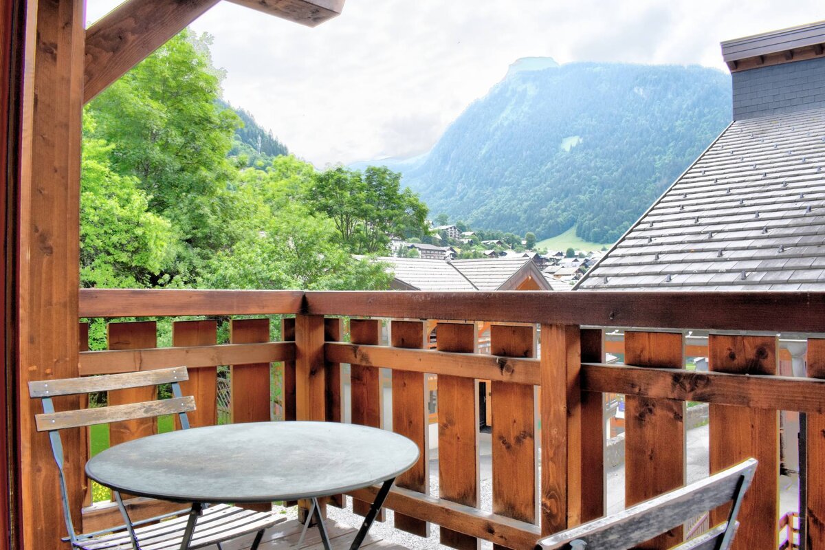 A balcony with a table and chairs and mountains in the background