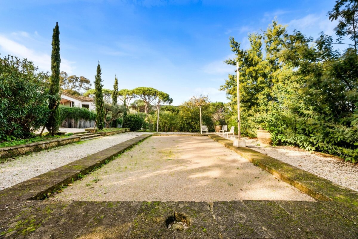 An outdoor bocce court surrounded by green trees and cypress pines under a blue sky.