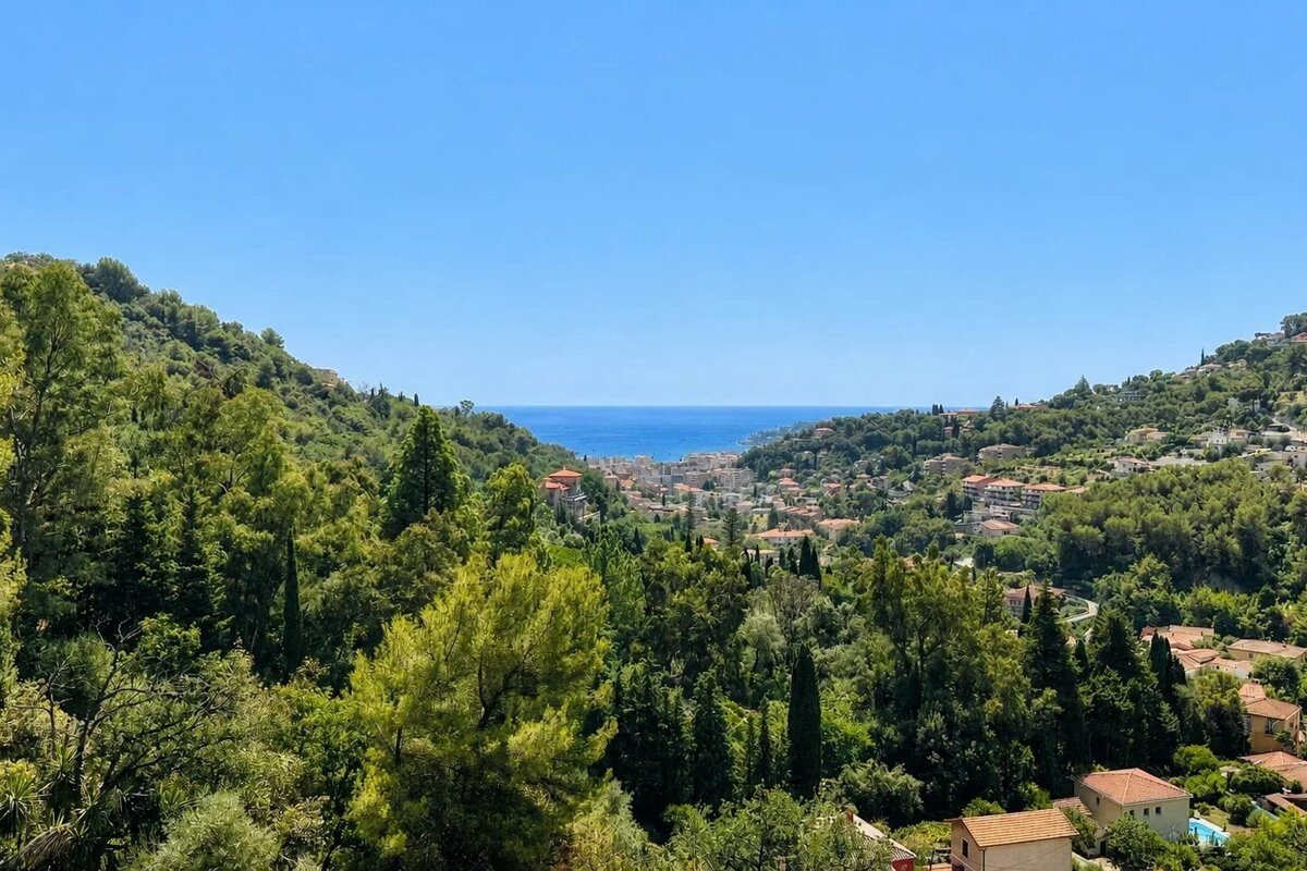 Lush green hills frame a distant coastal town and the bright blue sea under a clear sky.