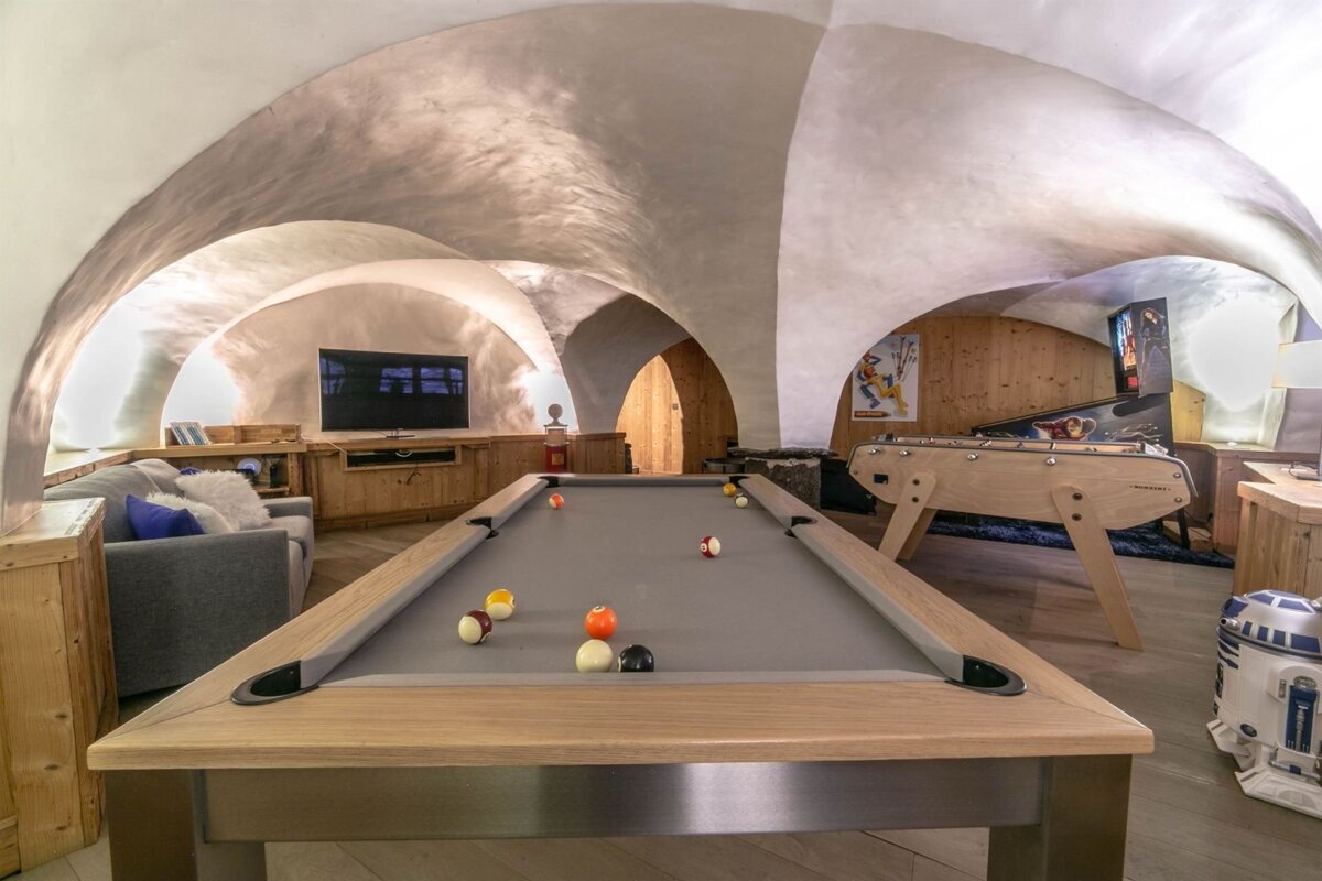 A stylish vaulted game room with a pool table, foosball, pinball machine, TV, sofa, and an R2-D2 figure.