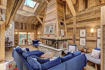 Cozy wooden chalet living room with plush blue sofas, a stone fireplace, and vaulted ceilings.