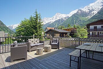 A deck with chairs and a table with mountains in the background
