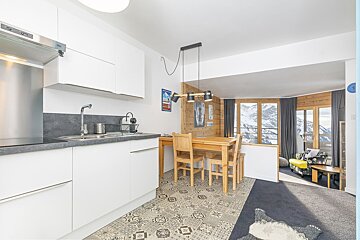 Modern kitchen, dining area, and living space with white cabinetry, a wooden table, and stunning snowy mountain views from large windows.