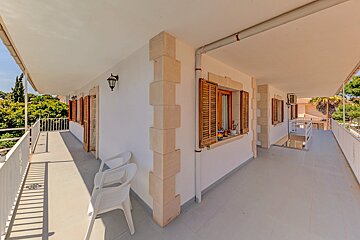 A balcony with white chairs and a window with shutters