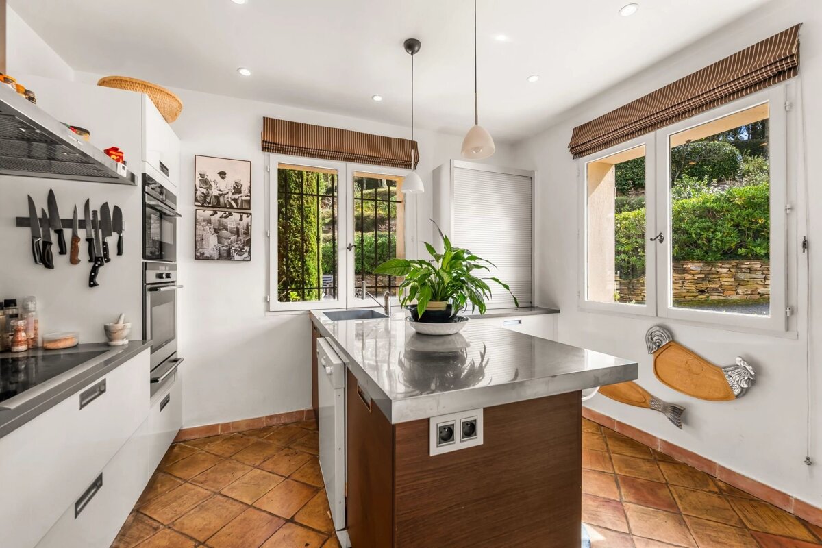 Bright kitchen with white cabinetry, terracotta floor tiles, and a central wooden island with a reflective stainless steel top.