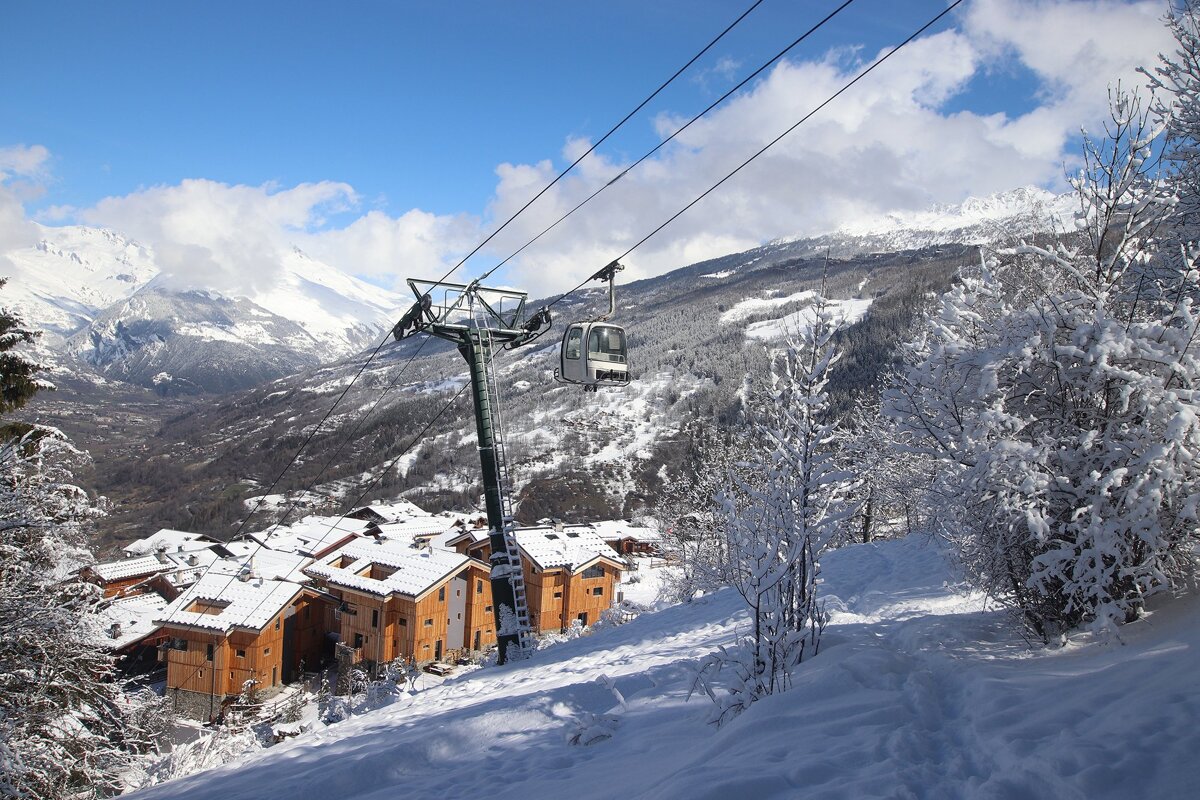 A ski lift going up a snowy hill with mountains in the background