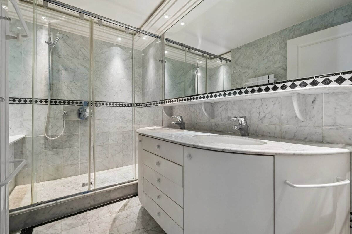 Modern bathroom featuring a marble-tiled glass shower, double vanity, and large wall-to-wall mirror.