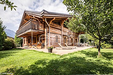 A large wooden house with a deck and chairs in front of it