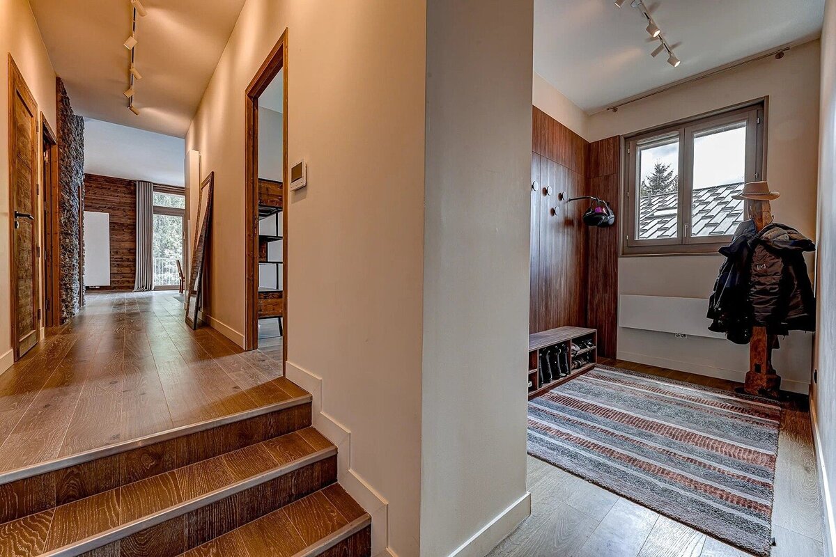 Inviting split-level home entryway with warm wood floors, steps, and paneling. Features a window, coat rack, and hallway leading to other rooms.
