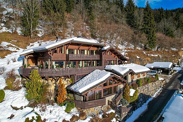 A large house is surrounded by snow and trees