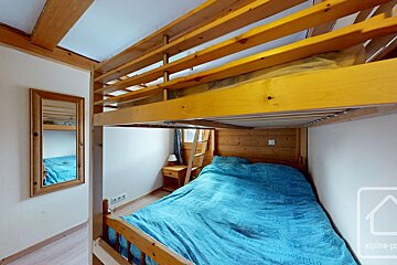 A rustic room with sturdy wooden bunk beds. A blue-covered bed is below, and a mirror hangs on the white wall.