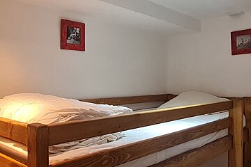 Rustic wooden bunk beds with crisp white bedding in a room with white walls and small red-framed artwork.