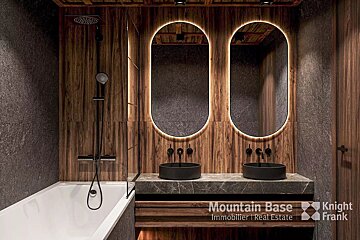 Modern bathroom with dark wood and gray stone walls. Features two backlit oval mirrors, black vessel sinks, and a white tub with dark fixtures.