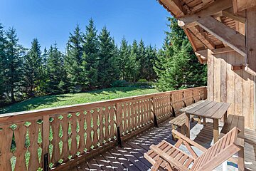 A wooden balcony with a table and chairs overlooking a forest