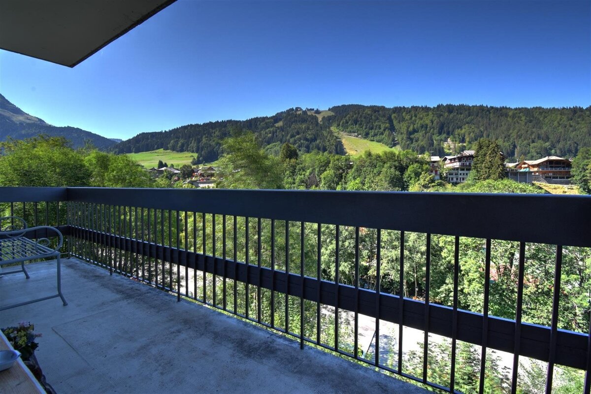 Balcony view overlooking a lush green valley and forested mountains under a clear blue sky.