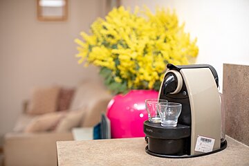 A krups coffee maker sits on a counter next to a vase of yellow flowers