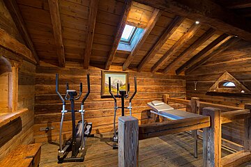 Rustic wooden attic gym with ellipticals, a massage table, and a skylight. This warm space features wooden walls, floor, and ceiling.